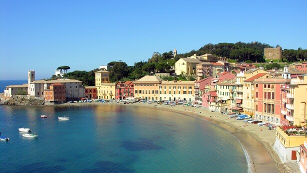 Un borgo costiero con edifici colorati, una spiaggia e barche in acqua.