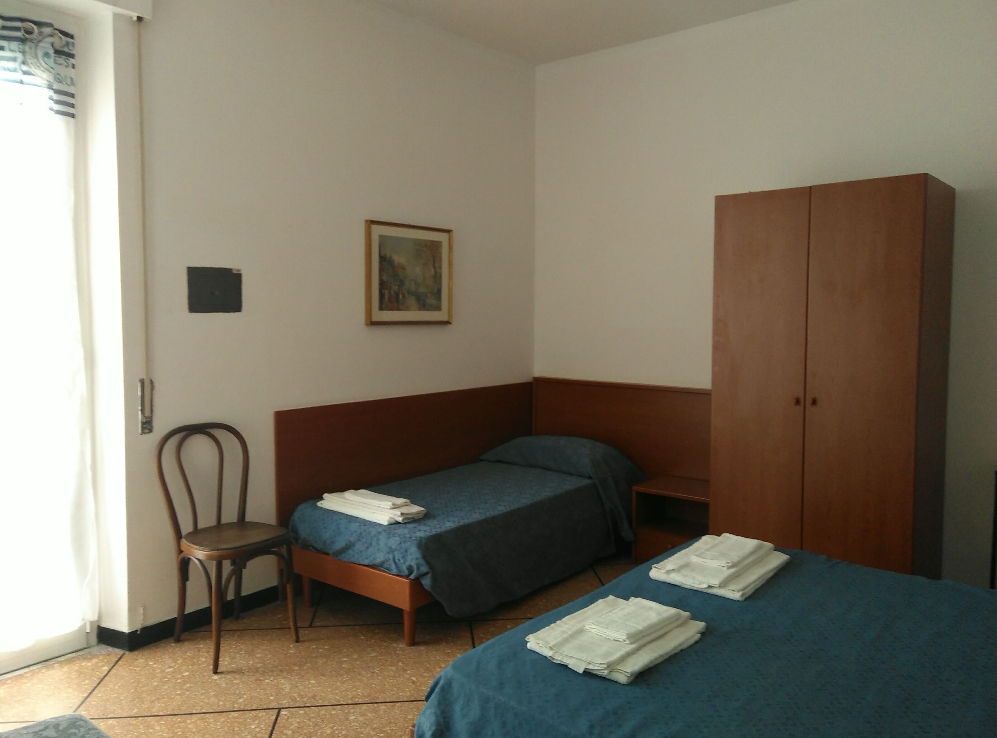 Una habitación pequeña y sencilla con dos camas, un armario de madera, una silla y un cuadro en la pared.