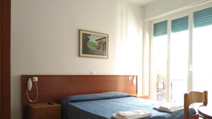 Una camera d'albergo con un letto di legno, un comodino, una sedia e un quadro appeso al muro.