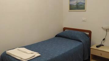 Un lit simple avec une couvre-lit bleue et une serviette blanche, une table de chevet avec une lampe et un tableau accroché au mur.