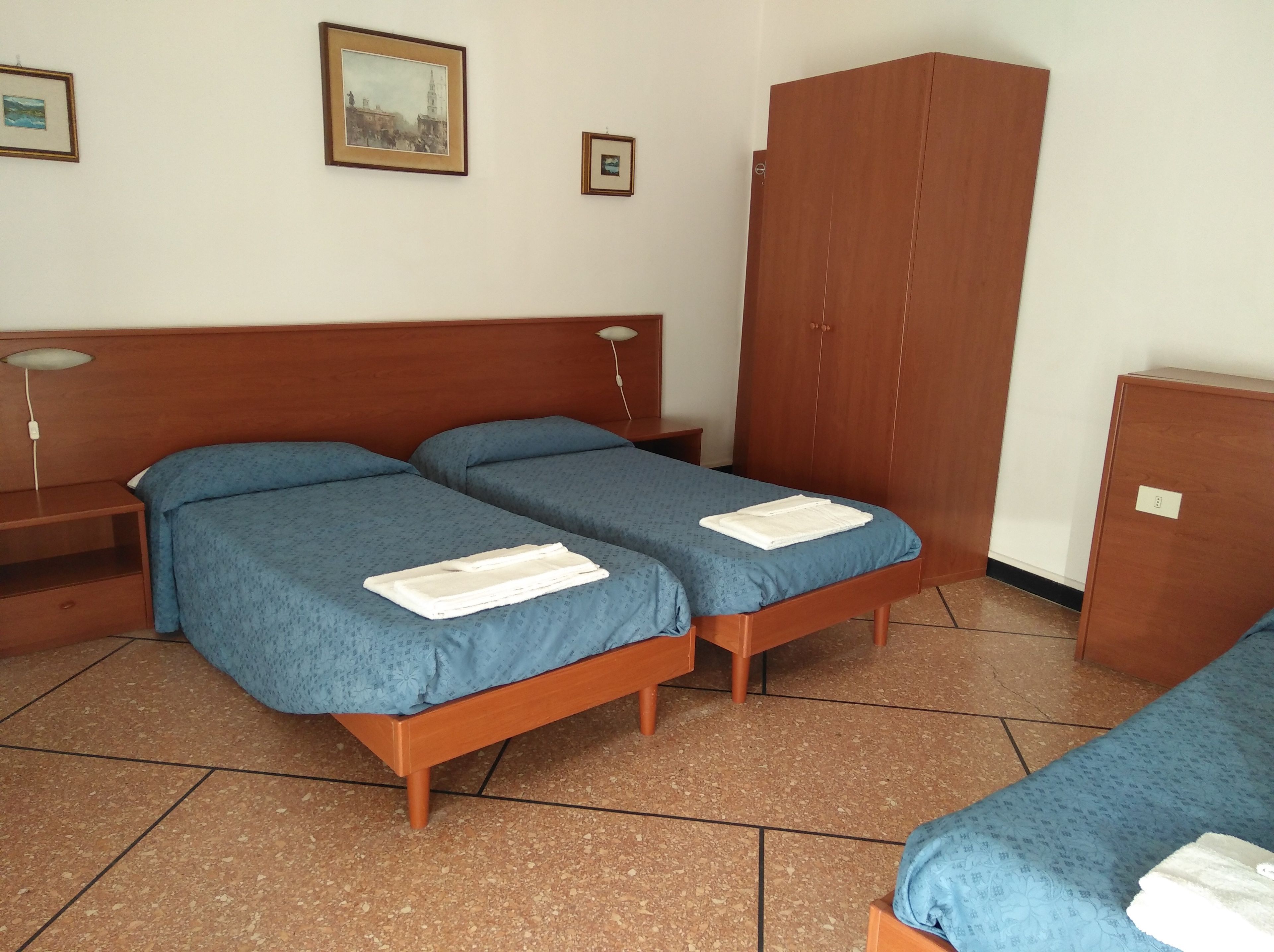 A room with two wooden beds, a wardrobe, and a desk with a lamp.