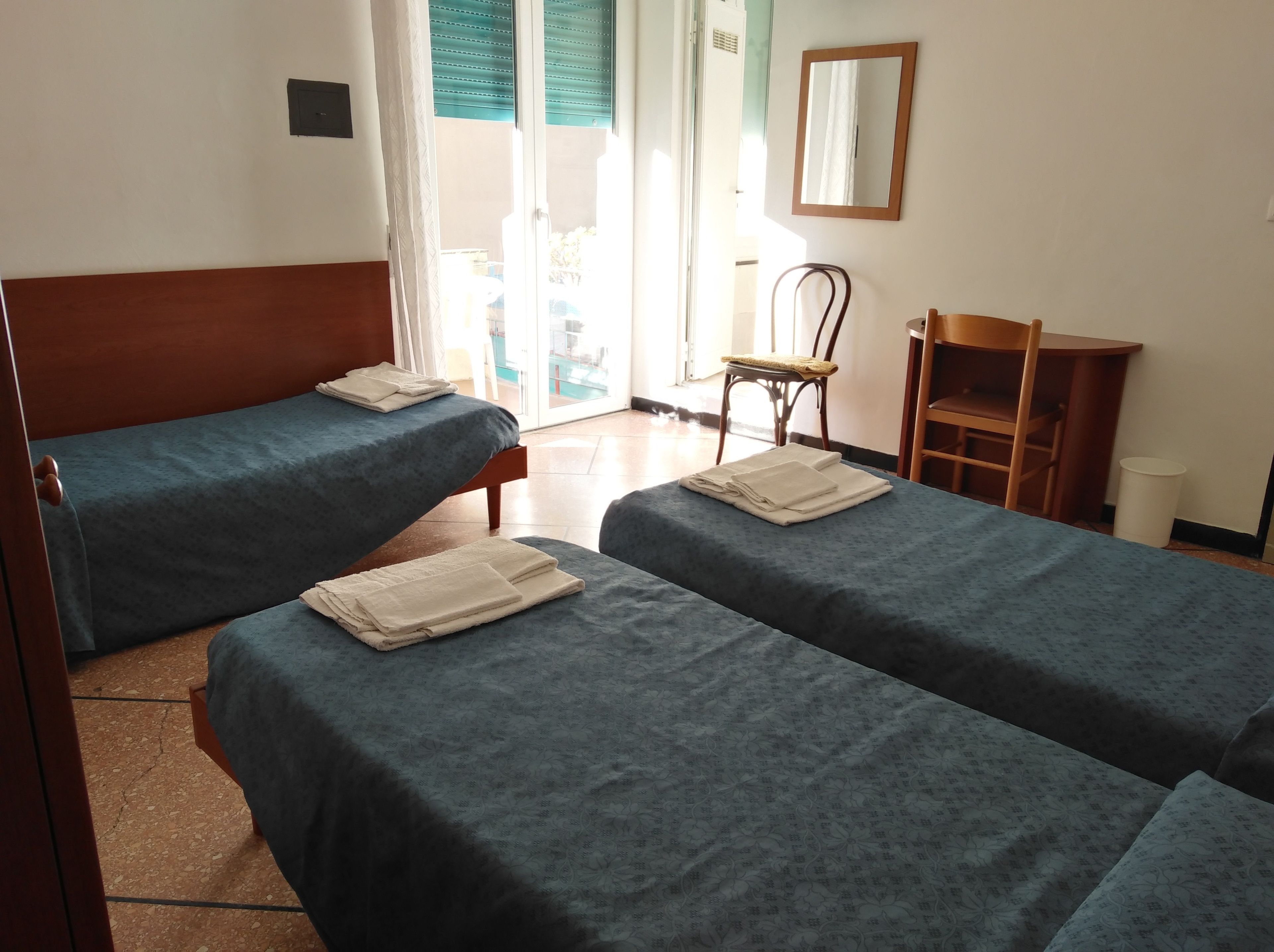 Une chambre d’hôtel avec deux lits simples, une chaise en bois, une petite table et une vue sur l’extérieur.