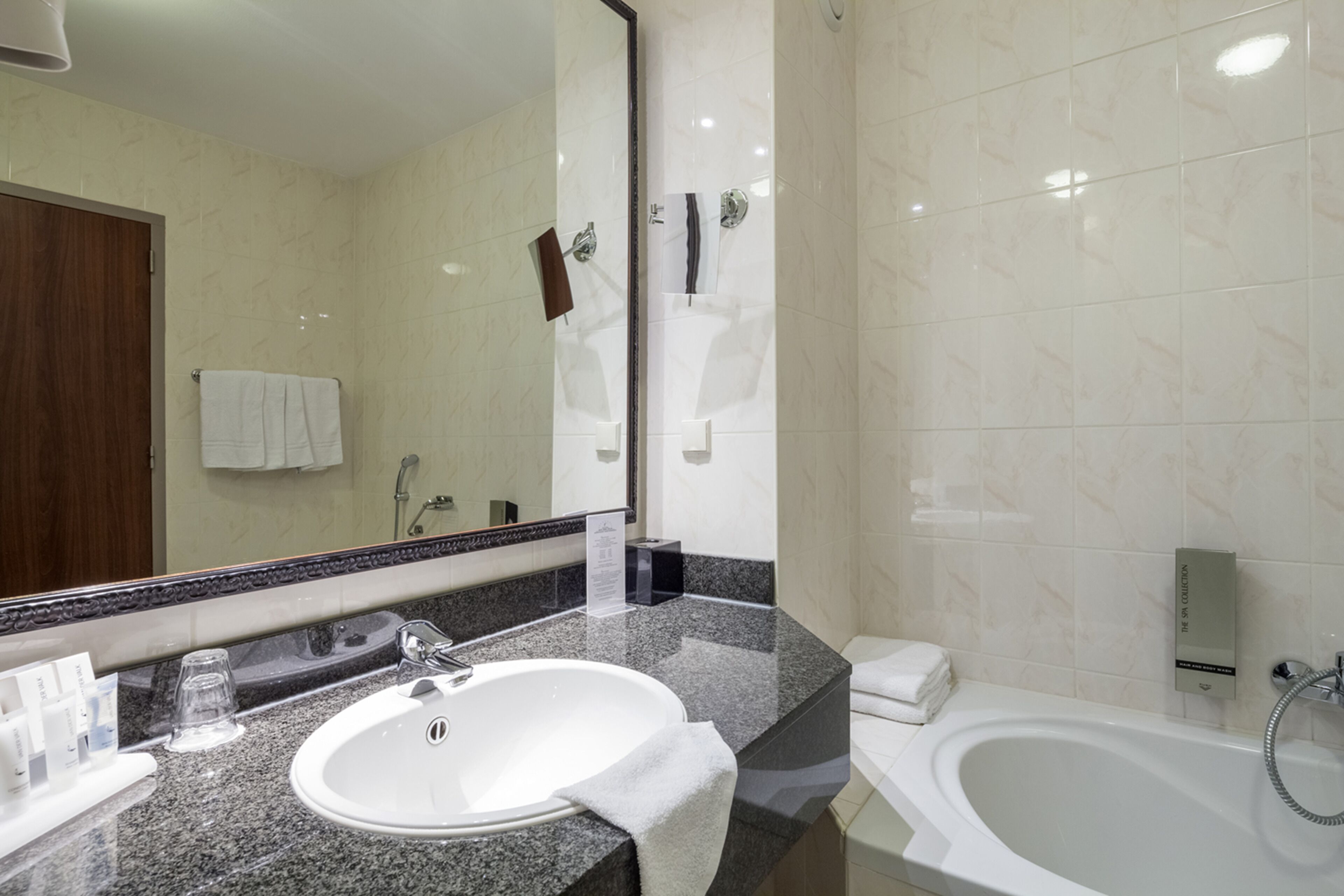 A modern bathroom with a granite countertop, a white sink, a large mirror, a bathtub, and a towel rack.