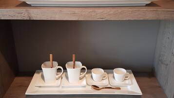 A coffee station with two trays of cups and spoons, a coffee maker, and a trash bin.