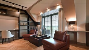 A modern living room with a herringbone wood floor, leather sofas, a white armchair, a coffee table, and a bookshelf. - Van der Valk Hotel Groningen Westerbroek (Westerbroek)