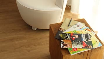 Un salon moderne avec un fauteuil blanc, une table basse en bois sur laquelle sont posés des magazines, un lampadaire blanc et une fenêtre avec des rideaux.