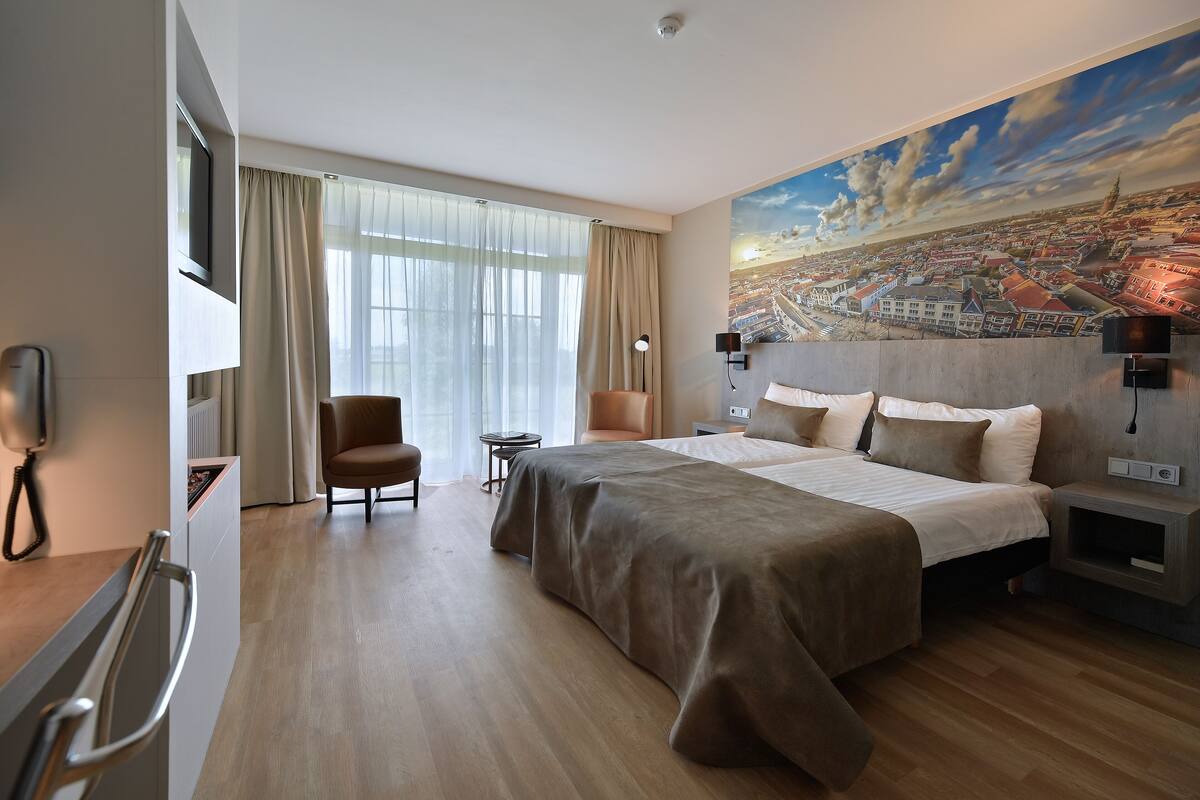 Habitación de hotel moderna con una cama grande, un escritorio, una silla y vistas a un mural de la ciudad.