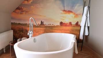 A modern bathroom with a freestanding bathtub, a radiator, and a large wall mural depicting a sunset over a field.