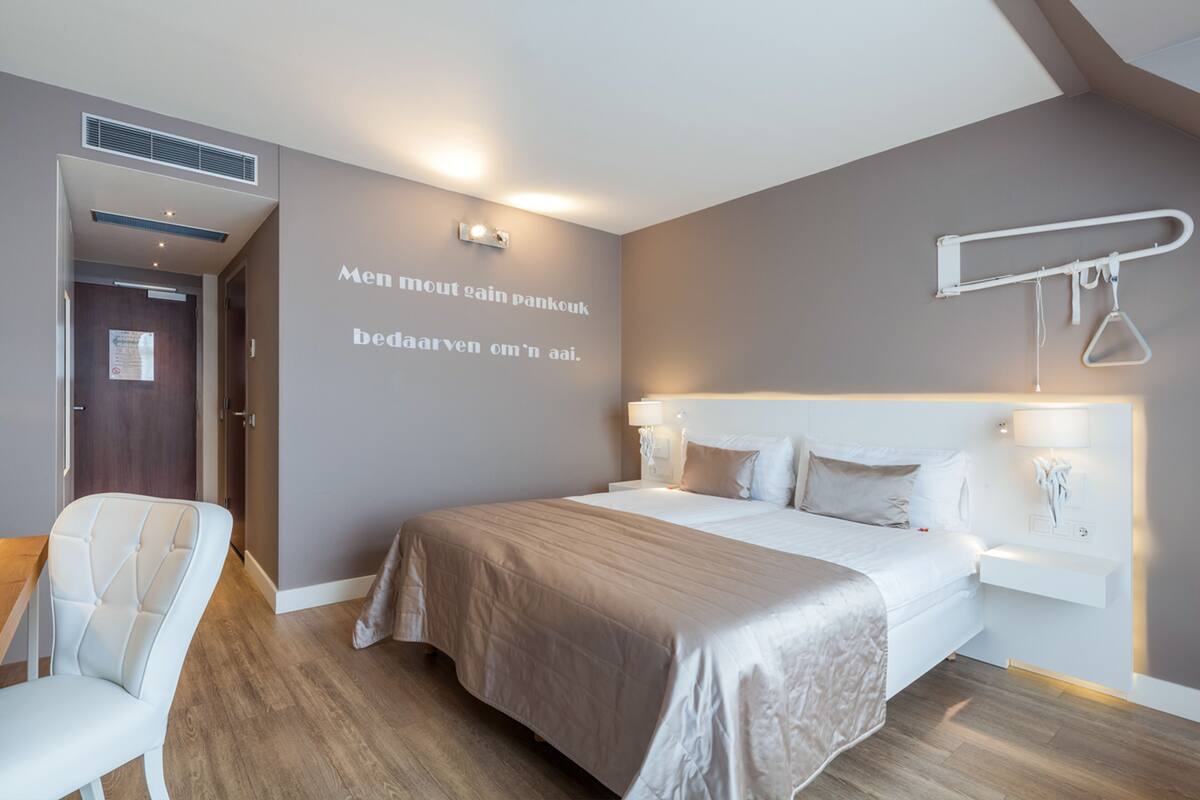 Una habitación de hotel moderna con una cama grande, mesitas de noche, una silla y un perchero en la pared.