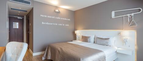 A modern hotel room with a large bed, bedside tables, a chair, and a wall-mounted towel rack.