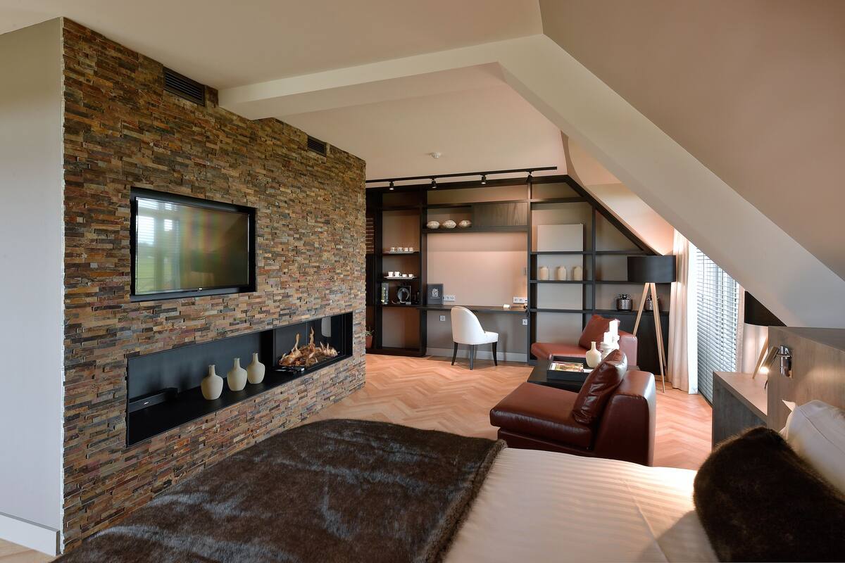 Un dormitorio moderno con chimenea de piedra, un televisor de pantalla plana, un sofá y una cama.