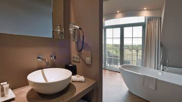 A bathroom with a large white sink, a freestanding bathtub, and a window with blinds.