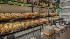 A bakery display with various breads and pastries, shelves with plants, and a counter with a candle. - Van der Valk Hotel Groningen Westerbroek (Westerbroek)