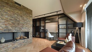 A modern living room with a herringbone wood floor, a stone fireplace, a leather sofa, and a black floor lamp. - Van der Valk Hotel Groningen Westerbroek (Westerbroek)