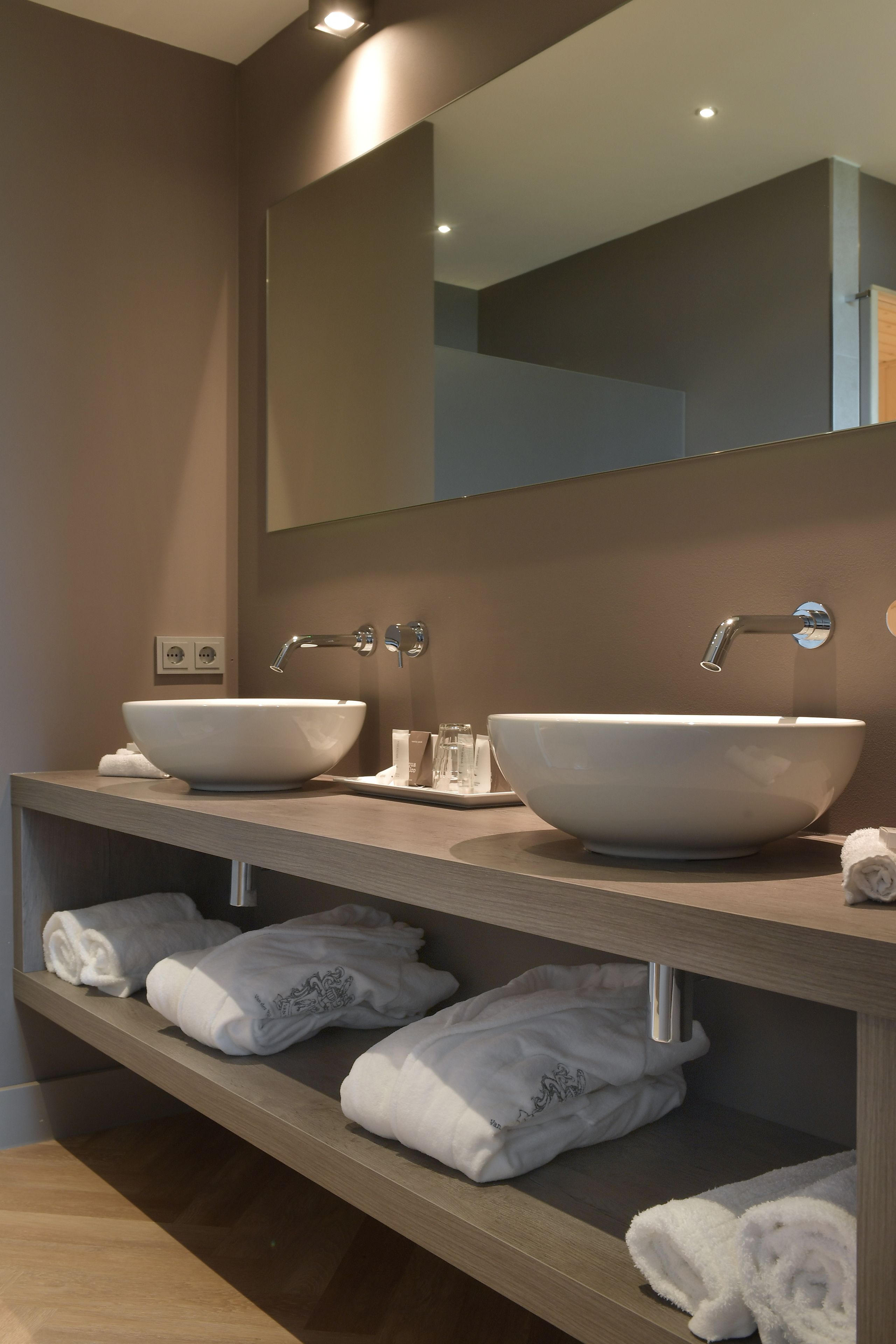 Een moderne badkamer met twee grote witte wasbakken, een spiegel en een plank met netjes opgevouwen handdoeken.