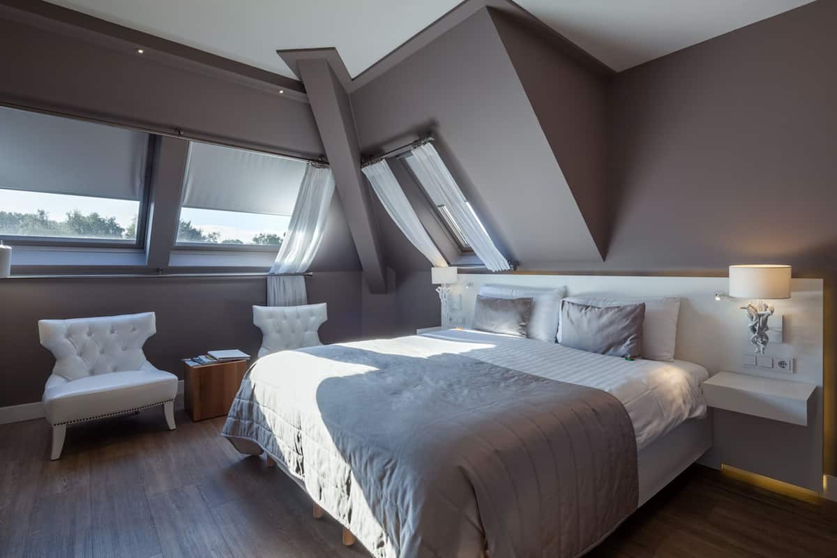 Un dormitorio moderno con una cama grande, dos mesitas de noche, una silla y una ventana con cortinas.