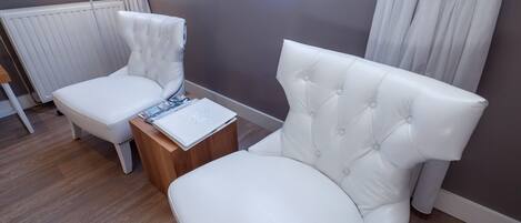 A modern bedroom with a white upholstered bed, a white armchair, and a wooden nightstand with a laptop.