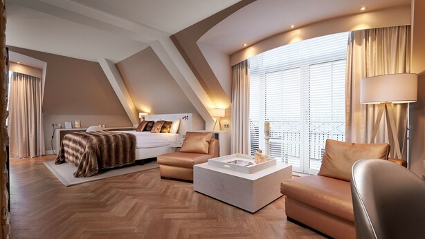 A modern hotel room with a loft-style ceiling, a large bed, a sofa, a coffee table, and a large window with curtains. - Van der Valk Hotel Groningen Westerbroek (Westerbroek)