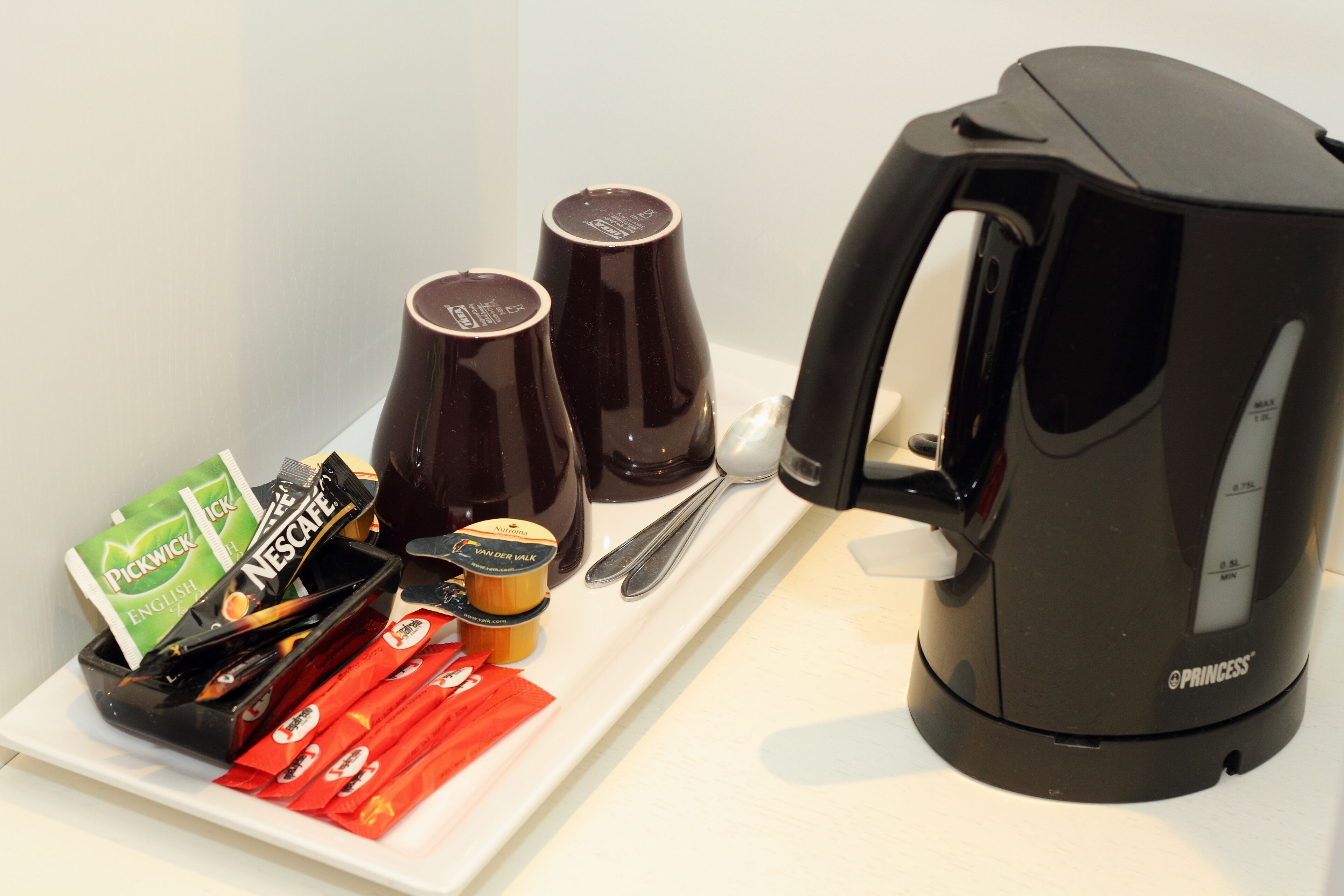 Een koffiezetapparaat, twee kopjes en een bord met koffiepads en een pakje melk.