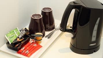 Een koffiezetapparaat, twee kopjes en een bord met koffiepads en een pakje melk.