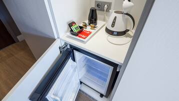 A kitchen area with a refrigerator, a coffee maker, and a kettle on the countertop.