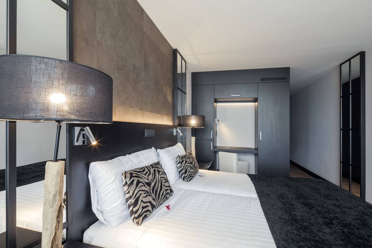 Una habitación de hotel moderna con una cama grande, un cabecero de madera, un escritorio y un armario.