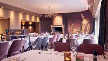 A restaurant with tables set for dining, a fireplace, and a large portrait on the wall.