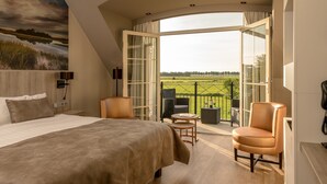 A bedroom with a large bed, a small table, two chairs, and a balcony with a view of a field. - Van der Valk Hotel Groningen Westerbroek (Westerbroek)