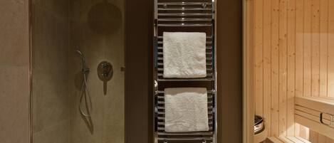 A bathroom with a shower, a towel rack with two towels, and a wooden sauna area.