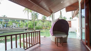 Terraza de madera con zona de estar acolchada con vistas a una piscina y abundante vegetación.