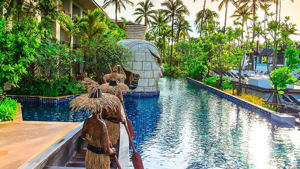 A pool area with a wooden deck, palm trees, and a stone structure in the background. - Graceland Khaolak Beach Resort (Takua Pa)