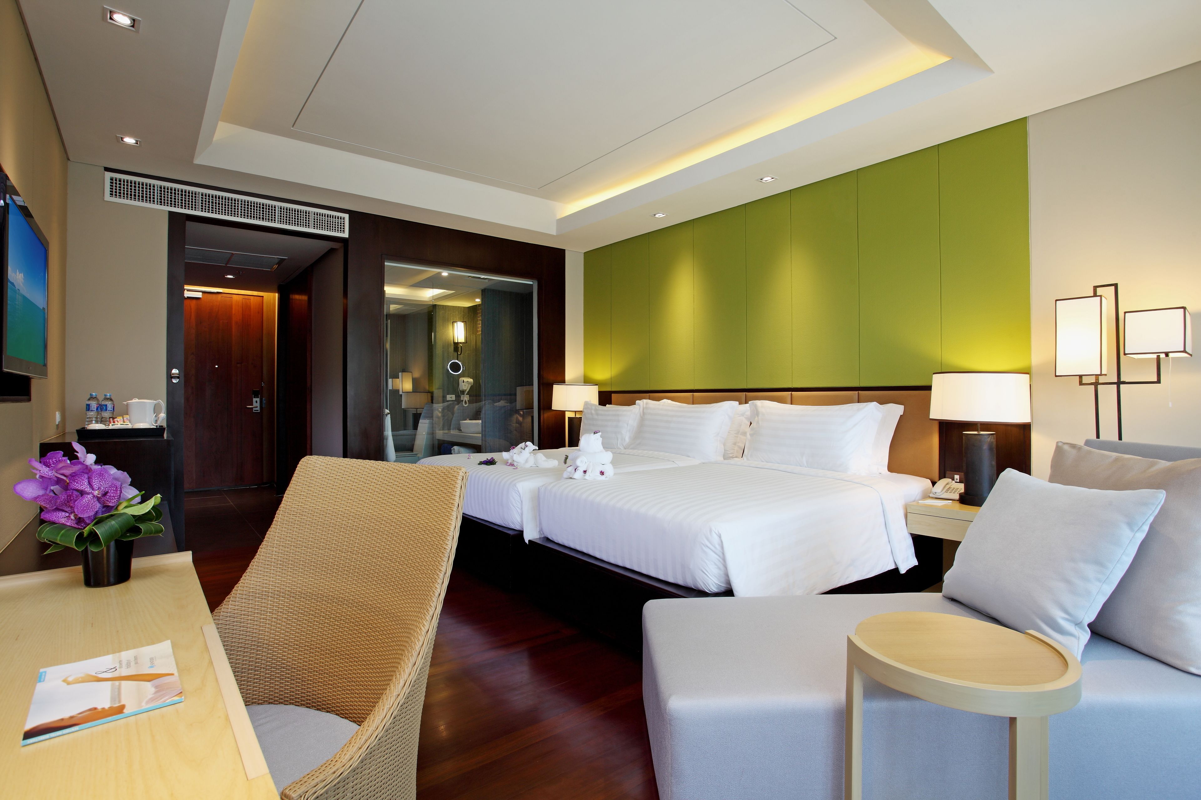 Une chambre d’hôtel avec un grand lit, deux tables de chevet, une chaise, une petite table et un mur d’accent vert.
