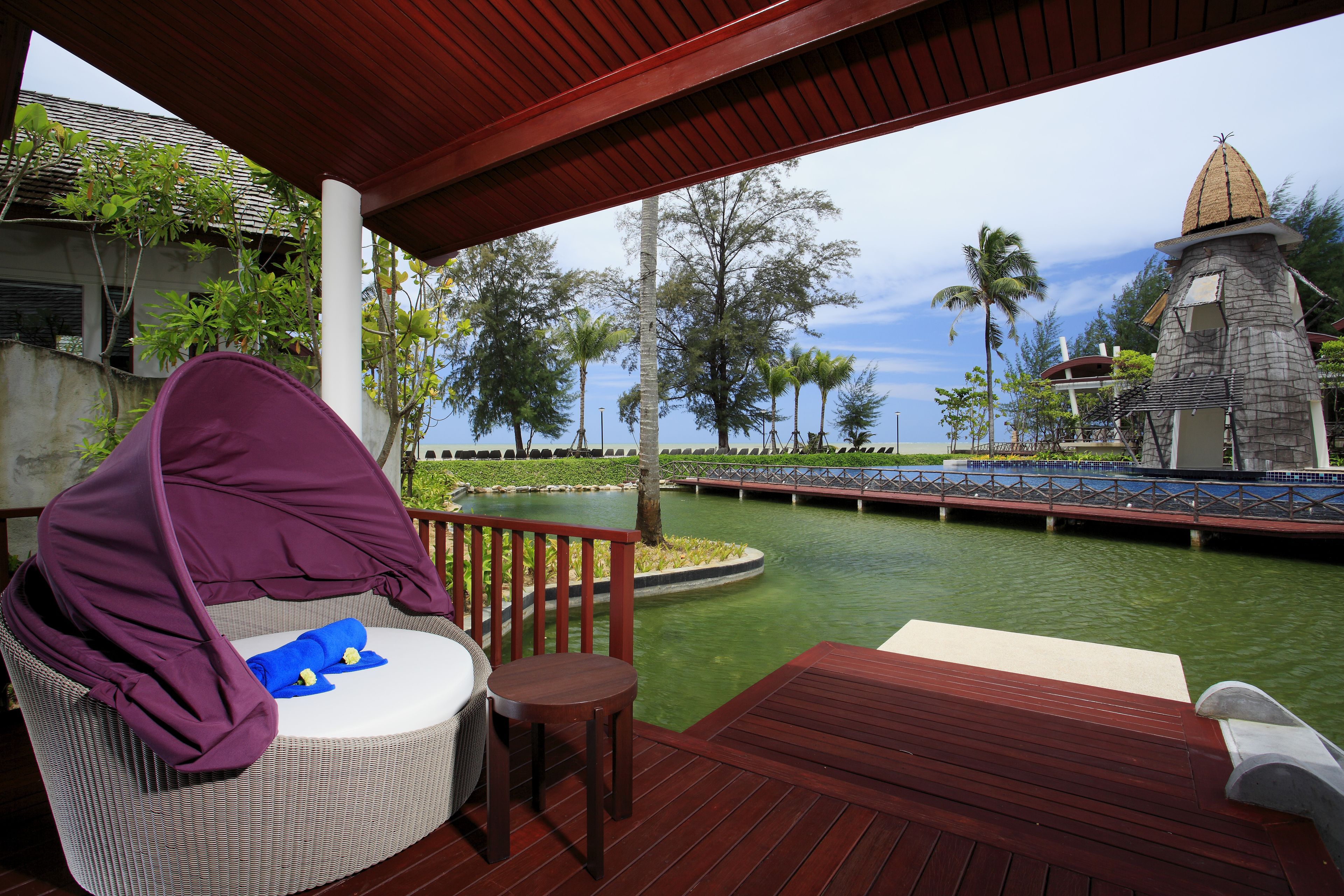 A covered outdoor seating area with a wicker chair and a small table, overlooking a water body and a bridge.