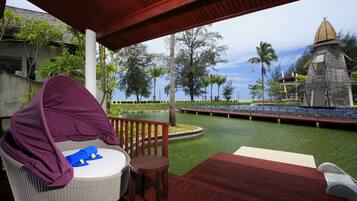 A covered outdoor seating area with a wicker chair and a small table, overlooking a water body and a bridge.