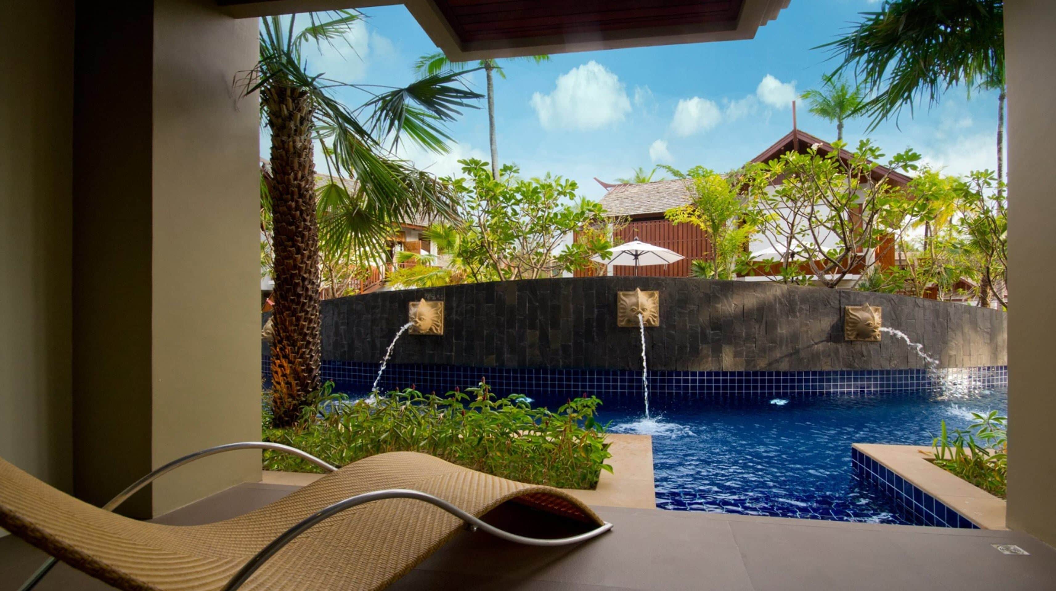 A pool area with lounge chairs, a stone wall, and tropical plants.