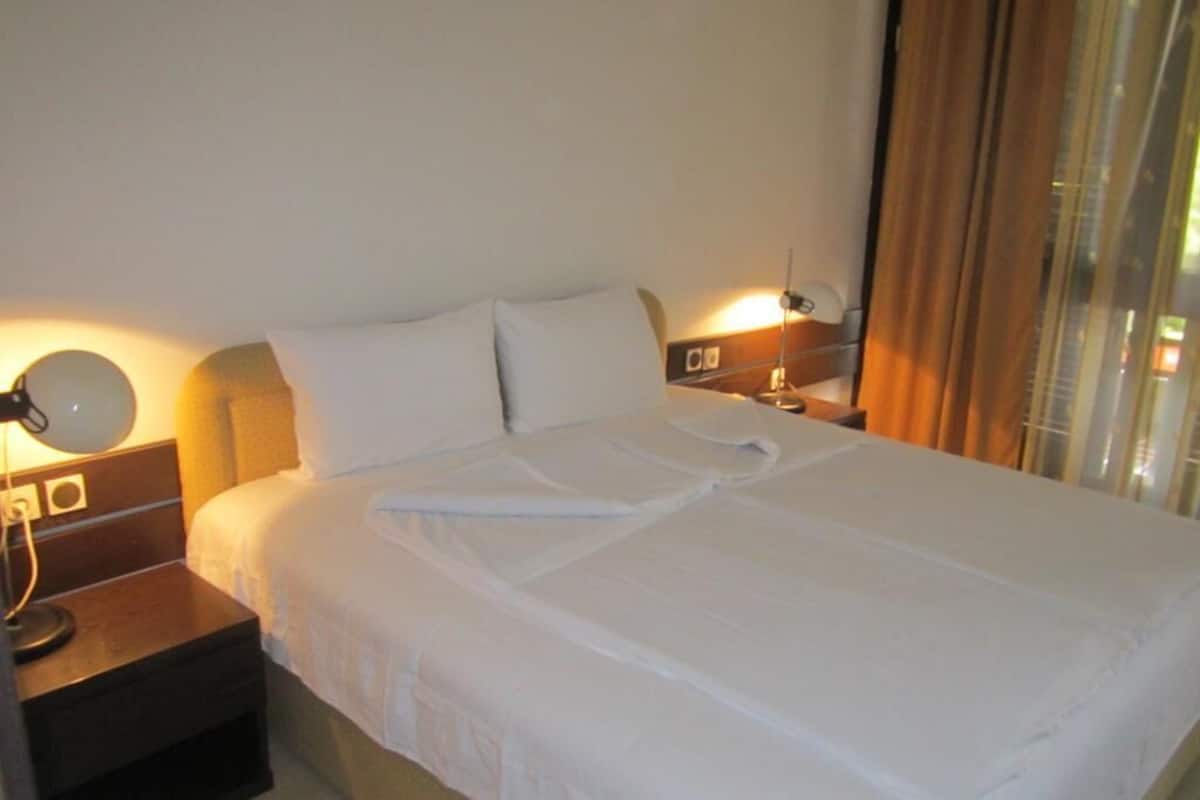 A neatly made bed with white linens, a bedside lamp, and a nightstand with a lamp.