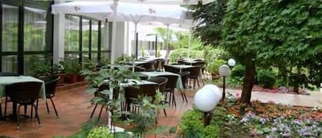 An outdoor dining area with tables and chairs, surrounded by greenery and flowers.