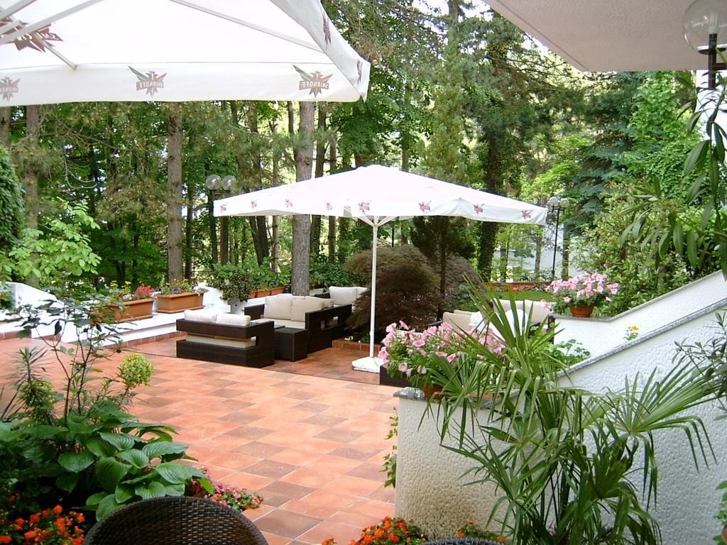 An outdoor patio area with a white umbrella, seating arrangements, and potted plants.