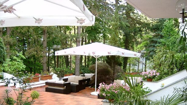 A covered outdoor patio with a seating area, surrounded by lush greenery and potted plants. - Pela Hotel Ohrid (Ohrid)
