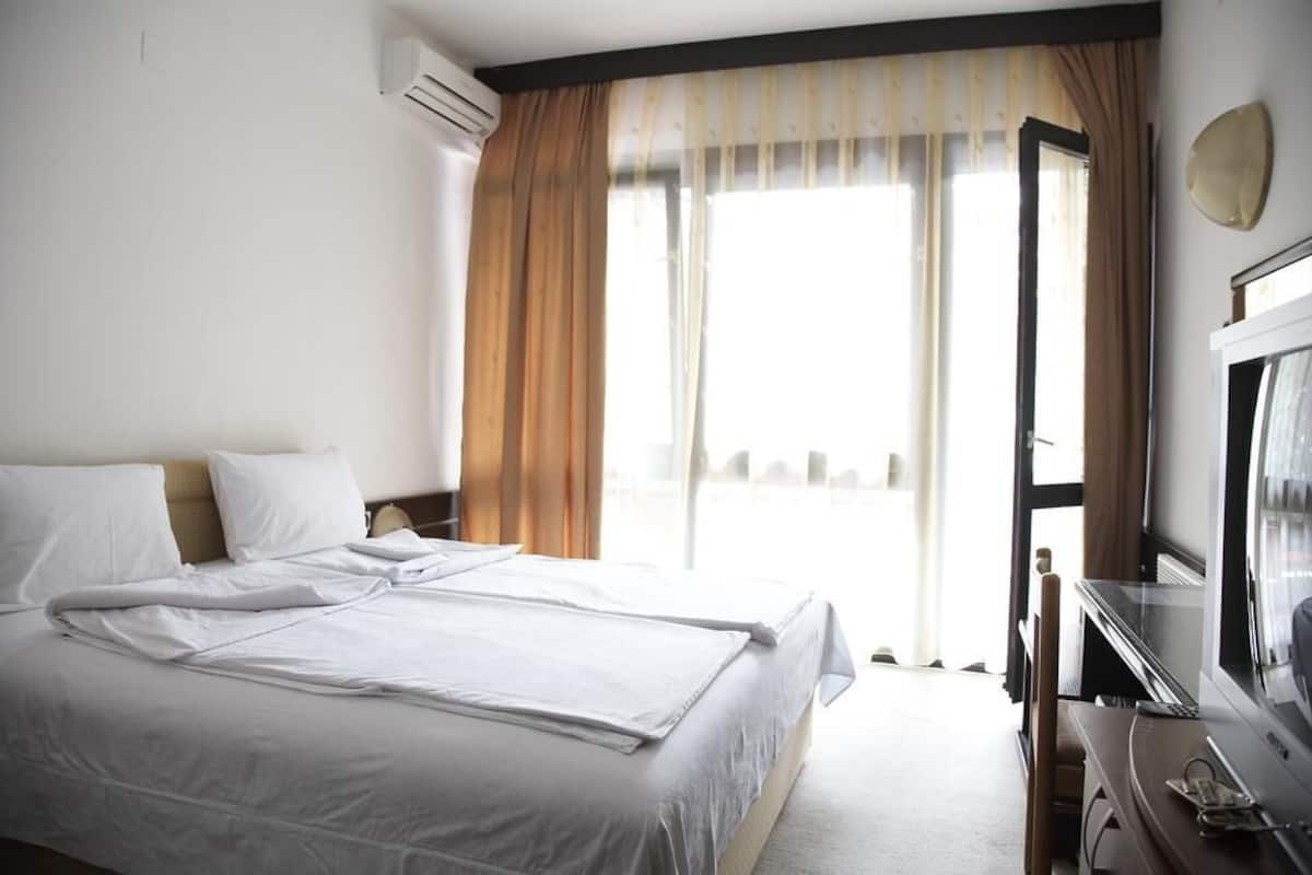 A hotel room with a large bed, a desk with a television, and a window with curtains.