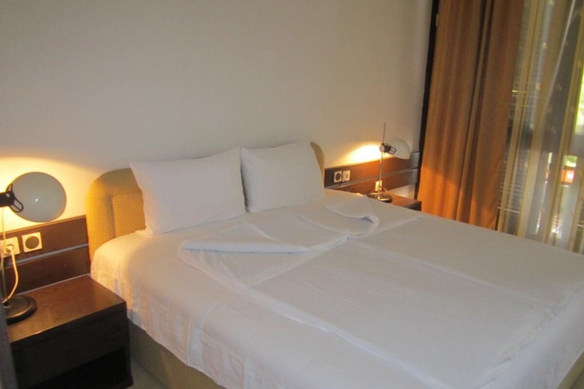 A hotel room with a neatly made bed, a bedside lamp, and a window with curtains.