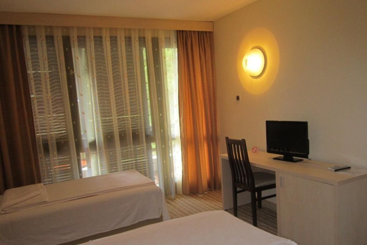 A hotel room with two beds, a desk with a chair, a television, and a window with curtains.