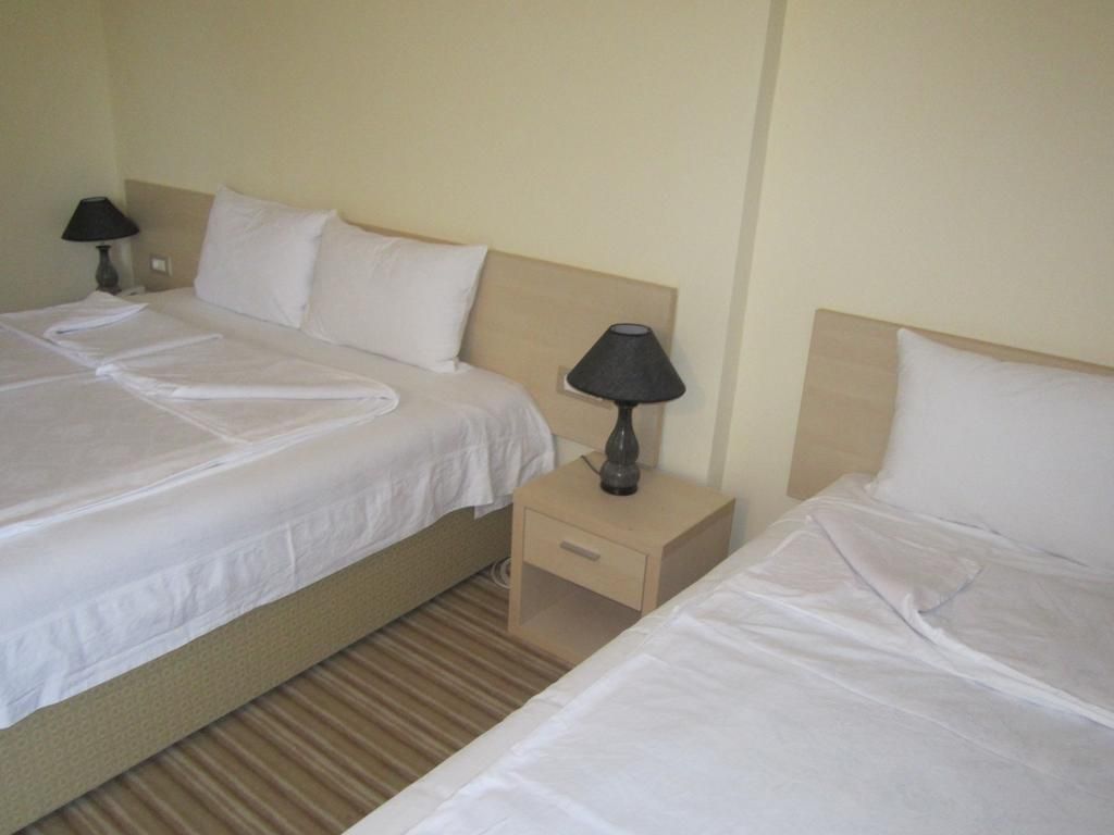 A hotel room with two single beds, each with a pillow and a bedside table with a lamp.