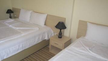 A hotel room with two single beds, each with a pillow and a bedside table with a lamp.