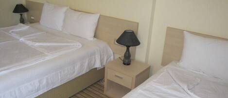 A hotel room with two single beds, each with a pillow and a bedside table with a lamp.