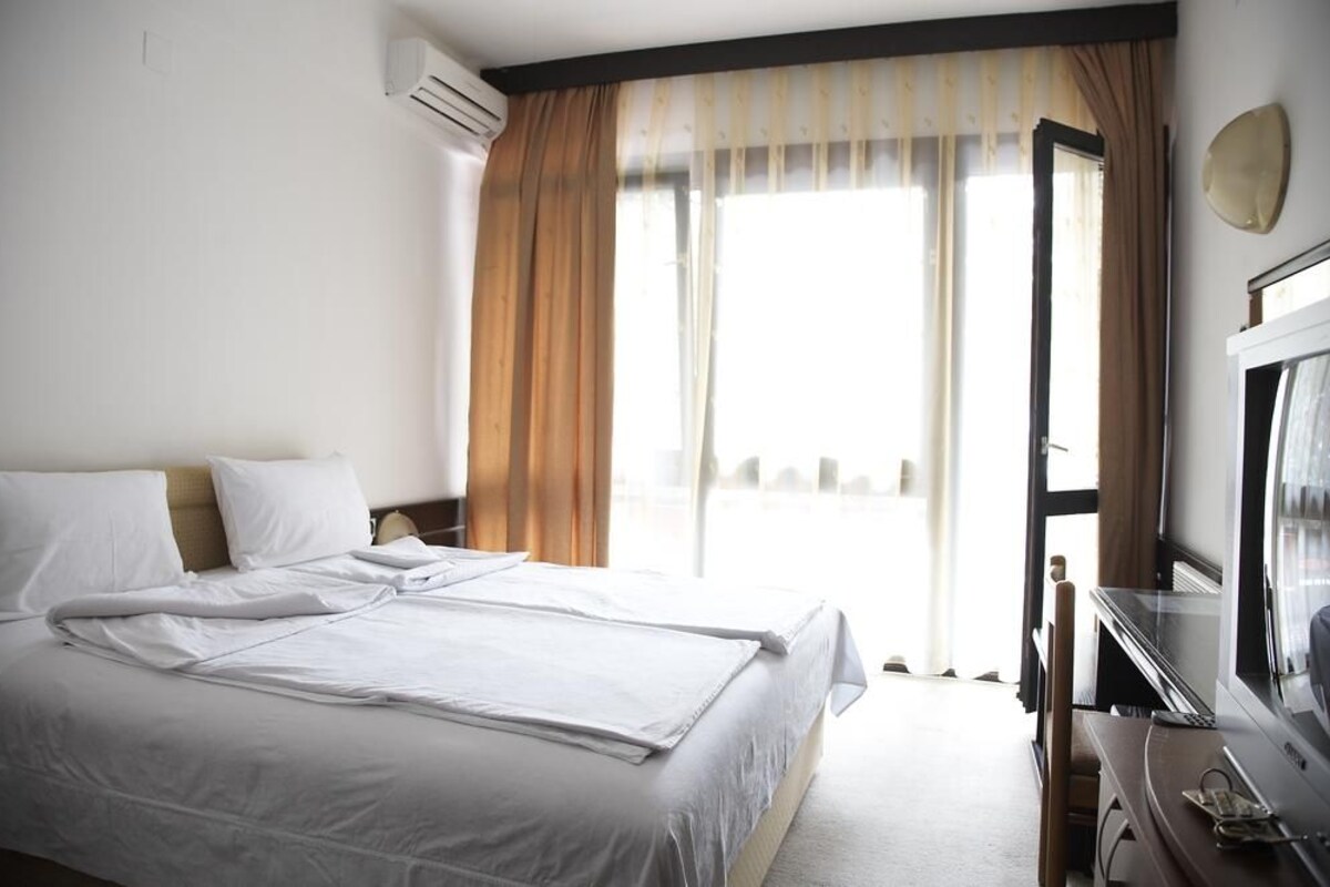 A hotel room with a bed, a desk with a television, and a window with curtains.