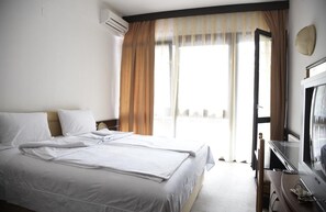 Ett hotellrum med en säng, ett skrivbord med en tv och ett fönster med gardiner.