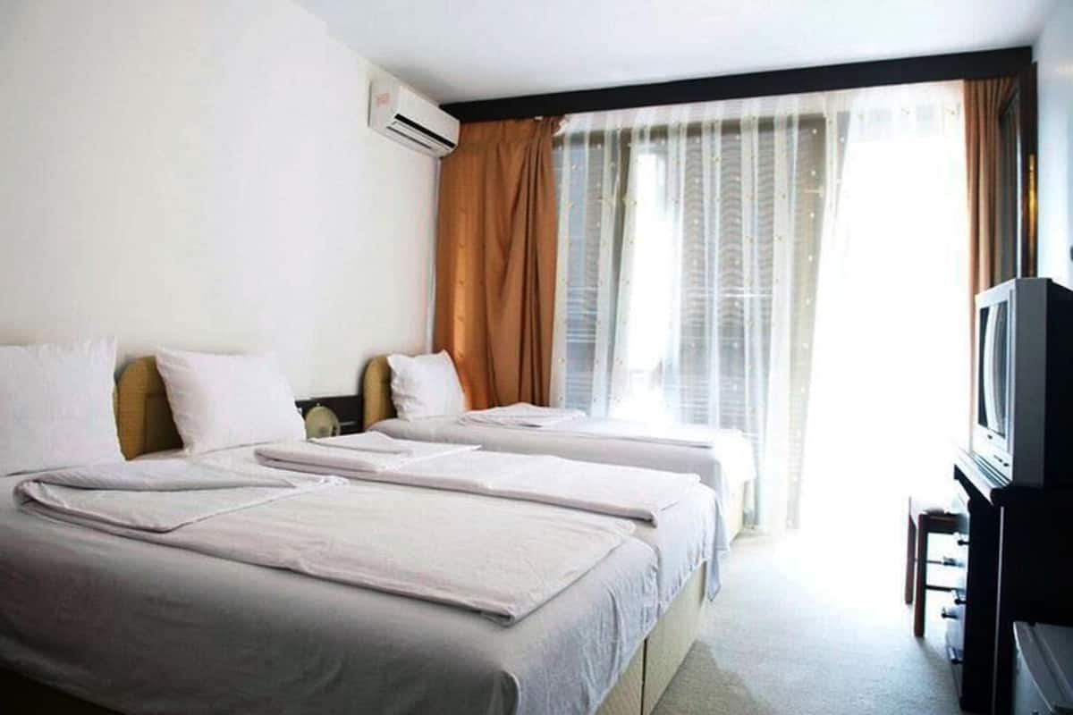 A hotel room with two beds, a television, and a window with curtains.