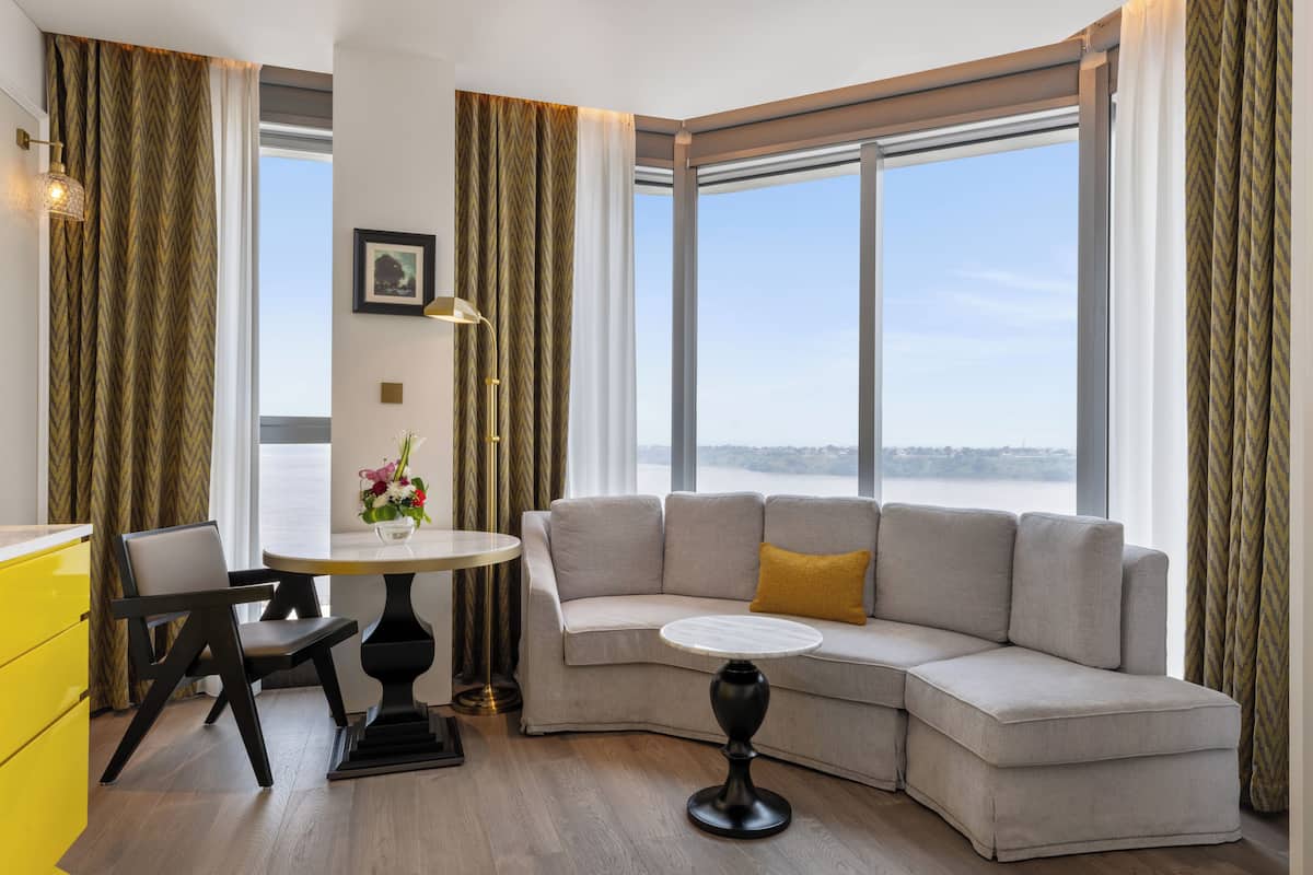 A modern living room with a curved sofa, a round dining table, and a view of the outdoors.