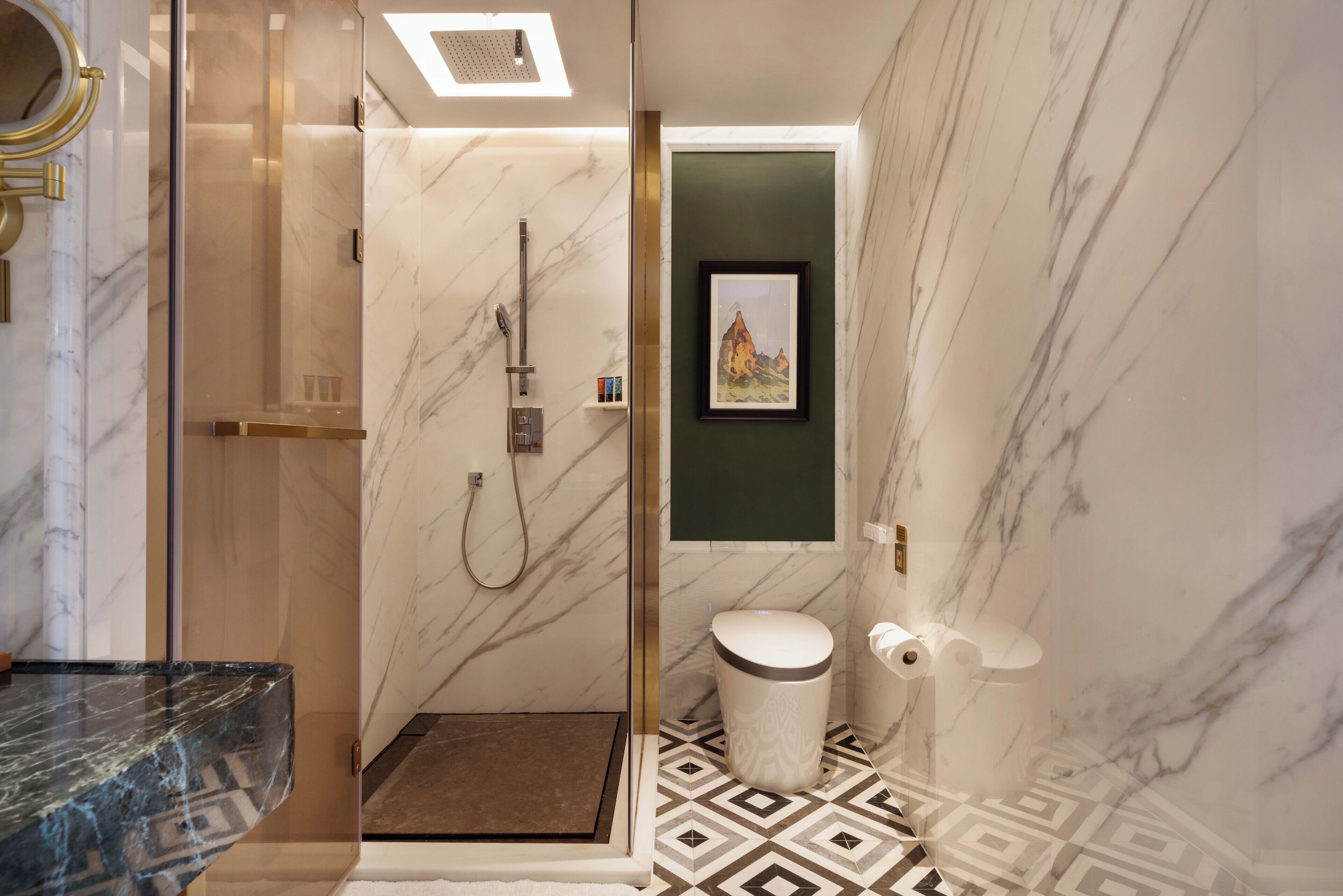 A modern bathroom with a glass-enclosed shower, marble walls, a geometric patterned floor, and a framed artwork on the wall.